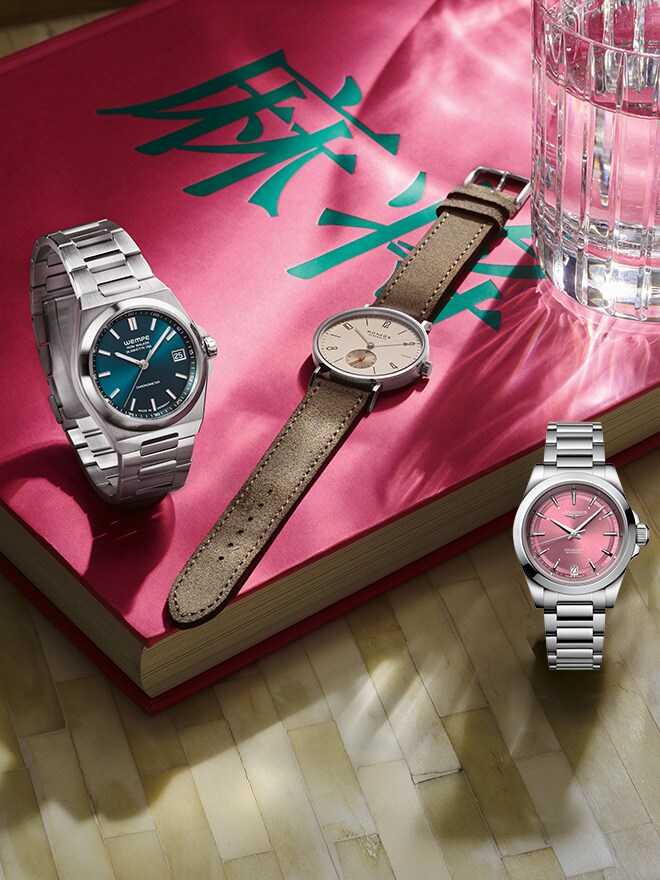 Longines Conquest, une Iron Walker Automatique Bleu Pétrole et une NOMOS Glashütte Tangente sur un livre rose avec des caractères chinois 