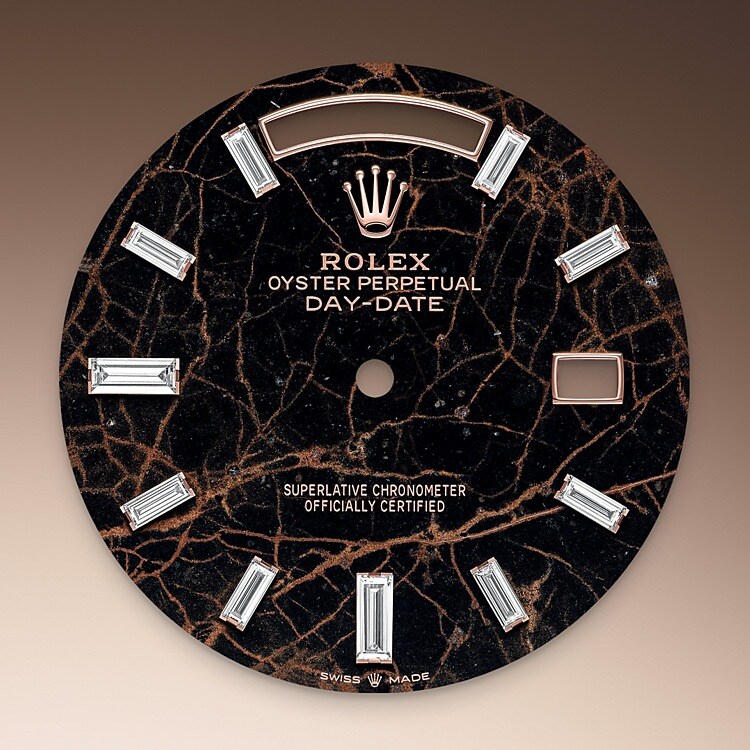 Ce cadran est doté de 10 diamants taille baguette. L’Oyster Perpetual Day‑Date 40 est présentée assortie d’un cadran eisenkiesel, une pierre ornementale brun profond utilisée par la marque pour la première fois en 2021. L’eisenkiesel est un quartz délicatement zébré de veines de fer oxydé. Les disques en pierre destinés aux cadrans sont taillés dans un bloc de matière brute. Seuls sont retenus ceux dont la ou les teintes et la structure répondent pleinement aux critères esthétiques très sélectifs de la marque. Ils viendront orner le cadran d’une montre Rolex, lui conférant une personnalité unique.