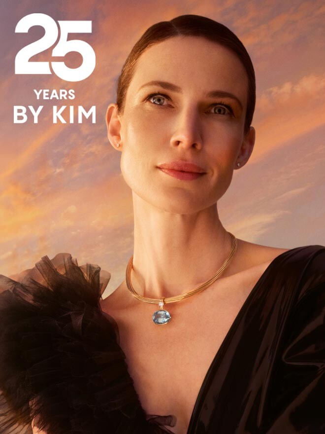 Frau im schwarzen Rüschenkleid trägt das Jubiläums Collier Helioro vor einem Sonnenuntergang, daneben das Jubiläumslogo 