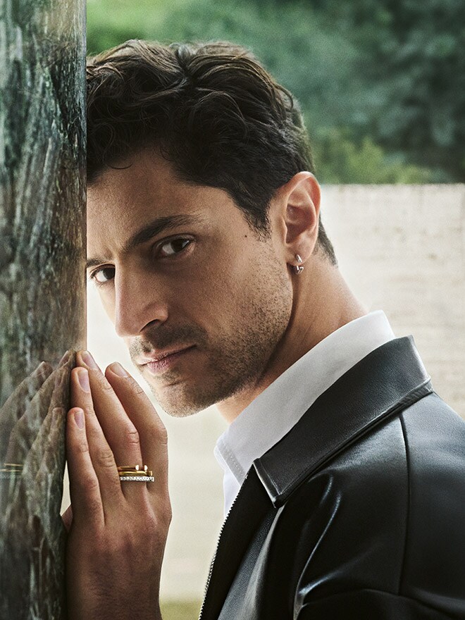Man in black leather jacket leaning against stone wall wearing rings and an earring from Atelier Wempe au:thentic