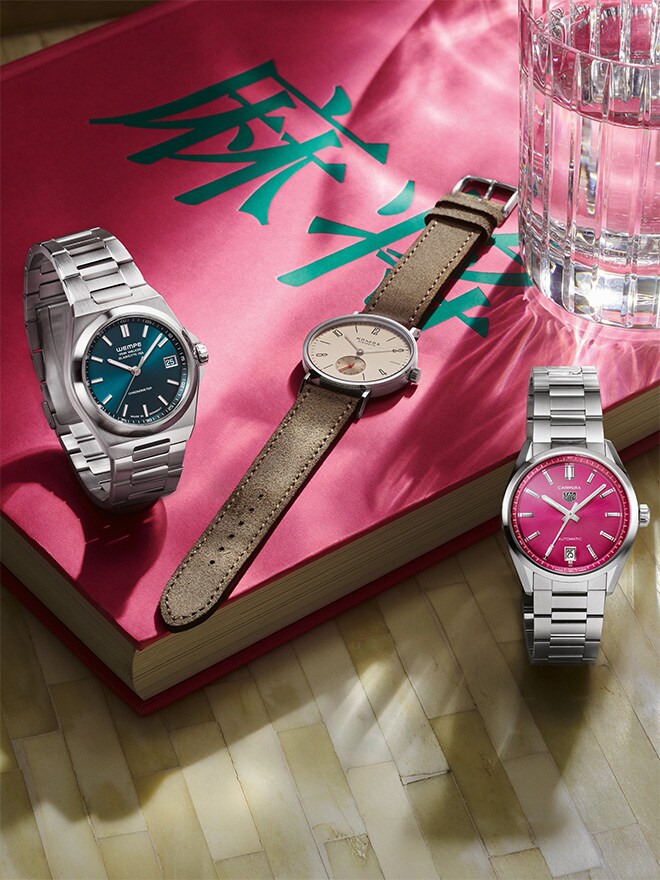TAG Heuer Carrera Date, Iron Walker Automatik Petrol, NOMOS Glashütte Tangente auf einem pinkfarbenen Buch mit chinesischem Schriftzeichen