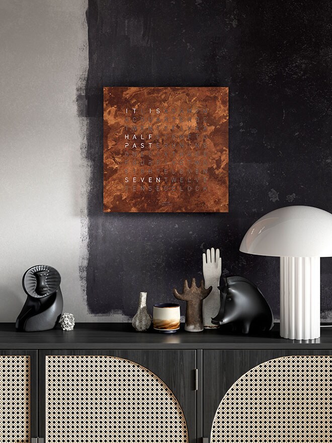 Model 45 Edition Rust by Qlocktwo on a black-painted wall above a sideboard with decorative items and a table lamp v
