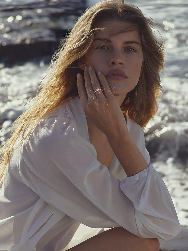 Blonde Frau in weißem Kleid kniet im Ozean und trägt einen Ring von WEMPE 137