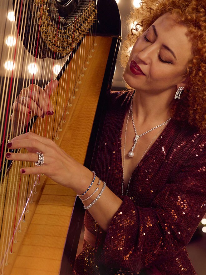 Frau mit roten Locken spielt Harfe und trägt Collier, Ohrringe und Ring der Linie Spotlight von High Jewelry sowie verschiedene Armreife